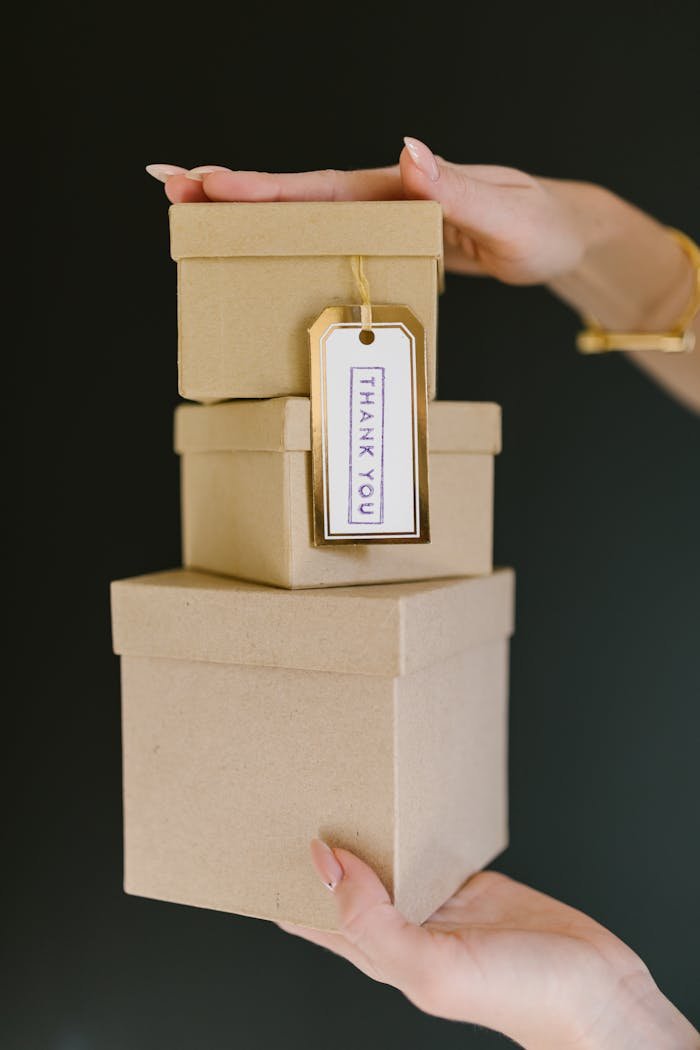 Three kraft gift boxes stacked with a Thank You tag held by a womans hands.